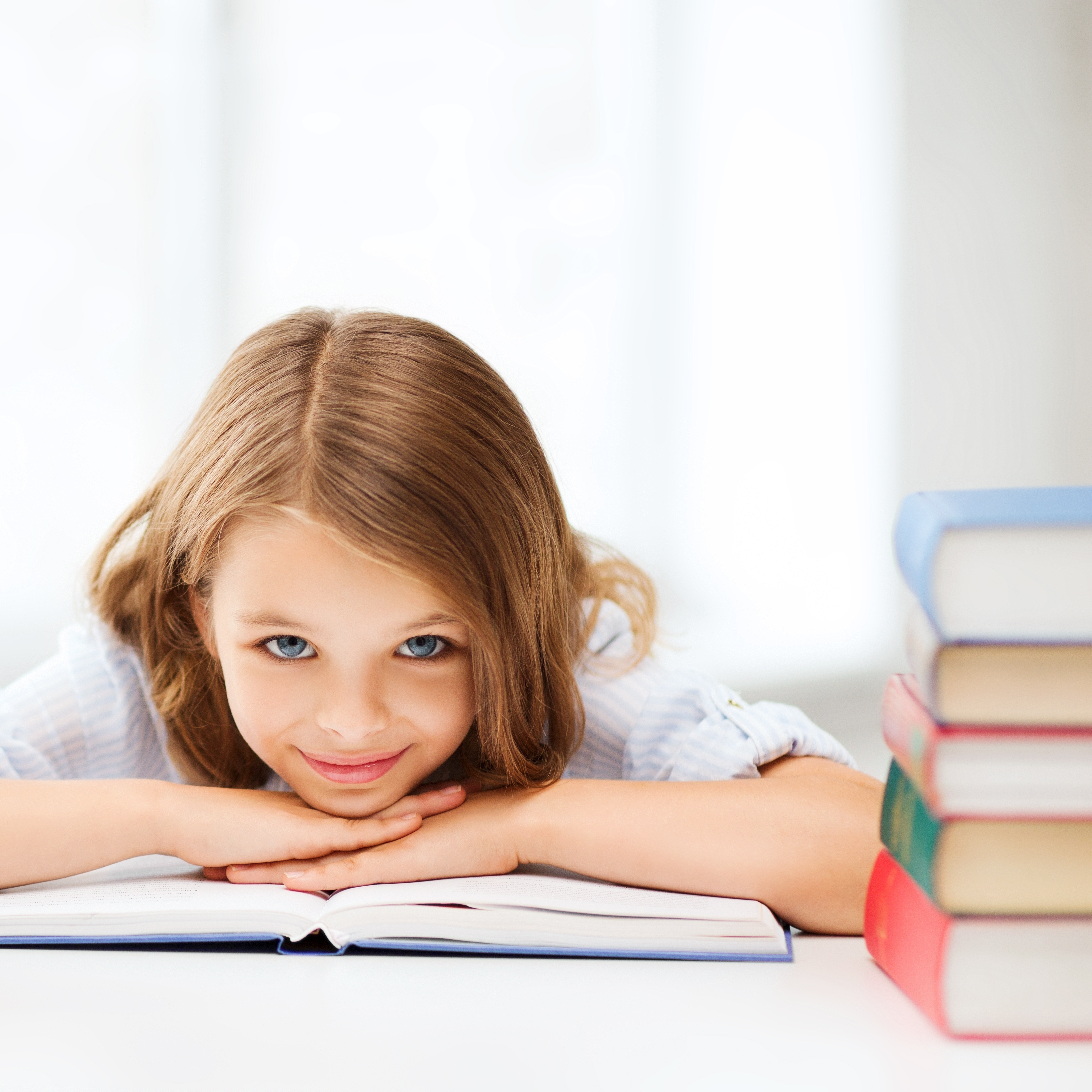 Ein Mädchen lächelt in die Kamera. Sie ist auf ein Buch gelehnt. Links von ihr steht ein Bücherstapel